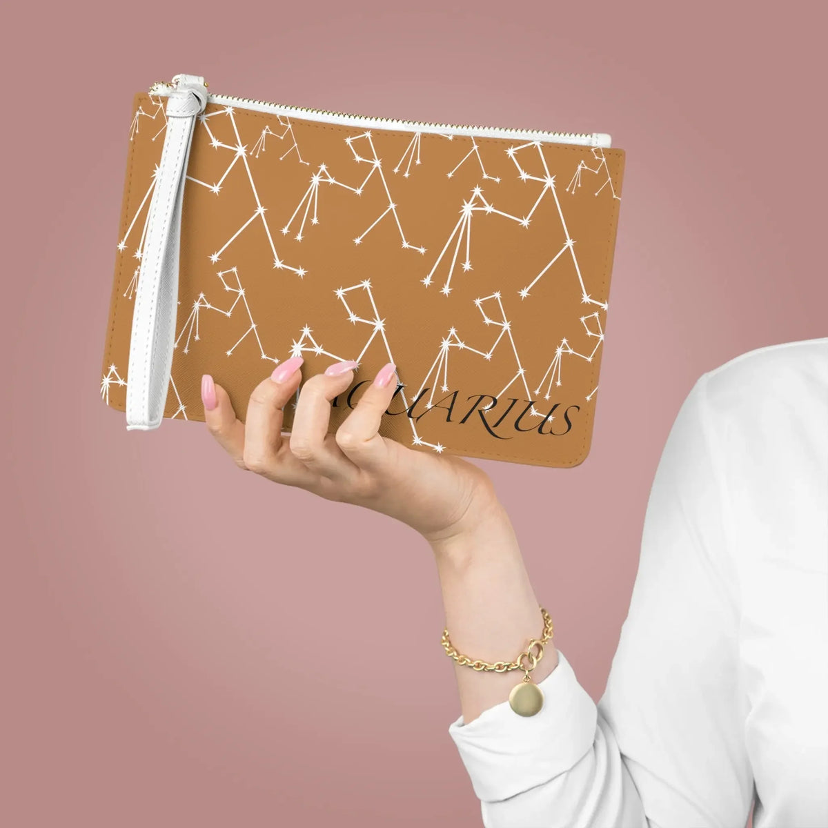 Brown Aquarius zodiac clutch with white constellation print, held by hand with pink nails