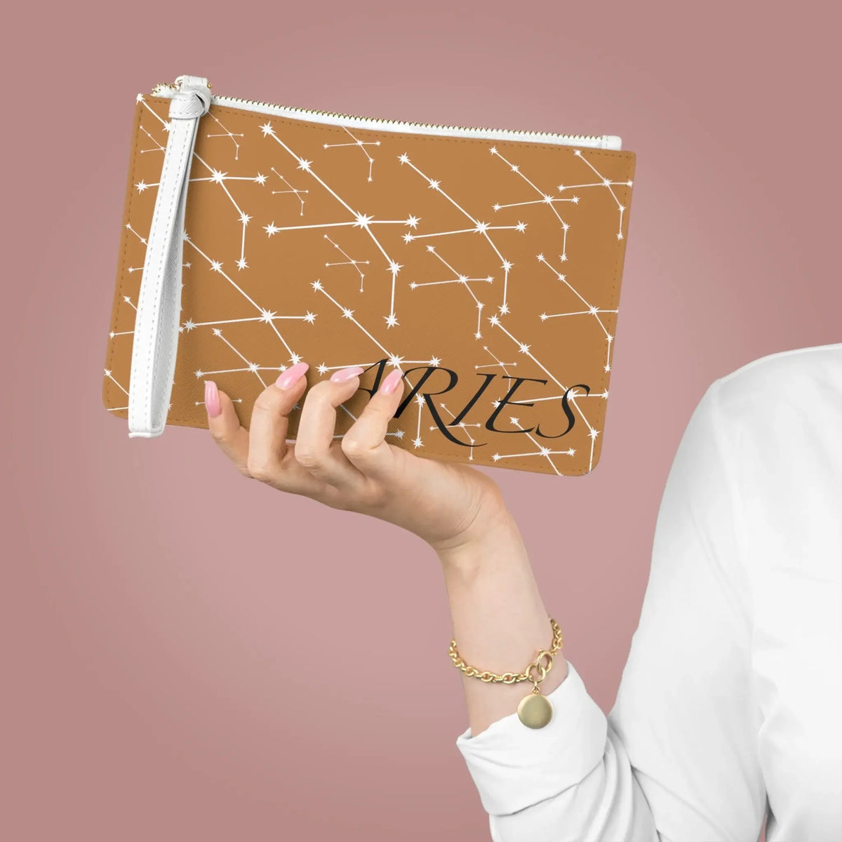 Aries zodiac constellation clutch bag with star pattern, held by hand with pink nails and gold bracelet
