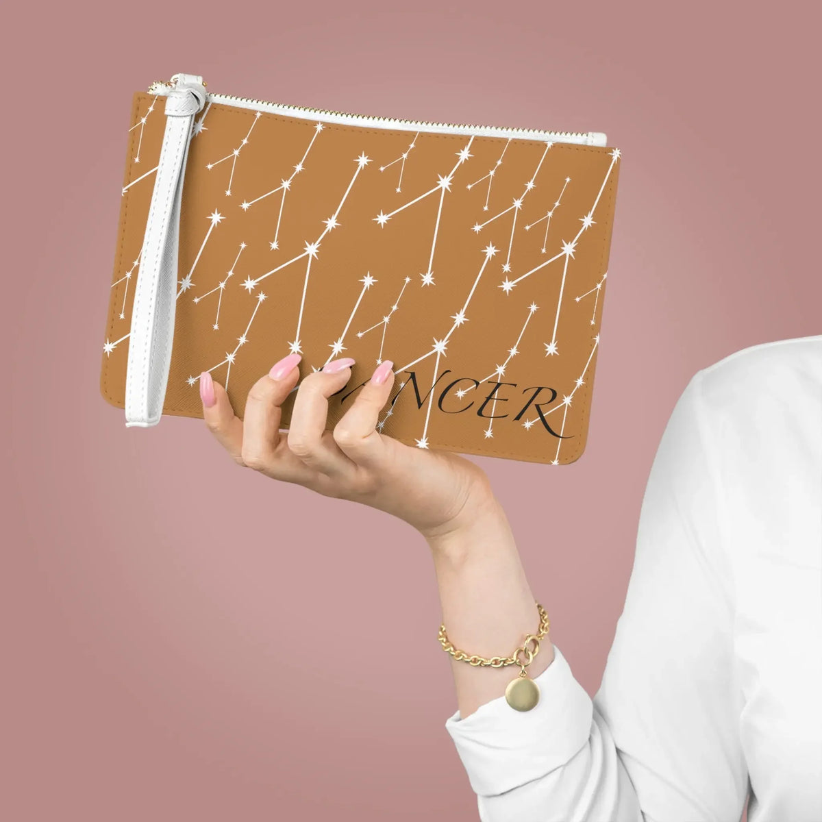 Tan Cancer zodiac clutch with white constellation stars, held by hand with pink nails, perfect for astrology lovers.