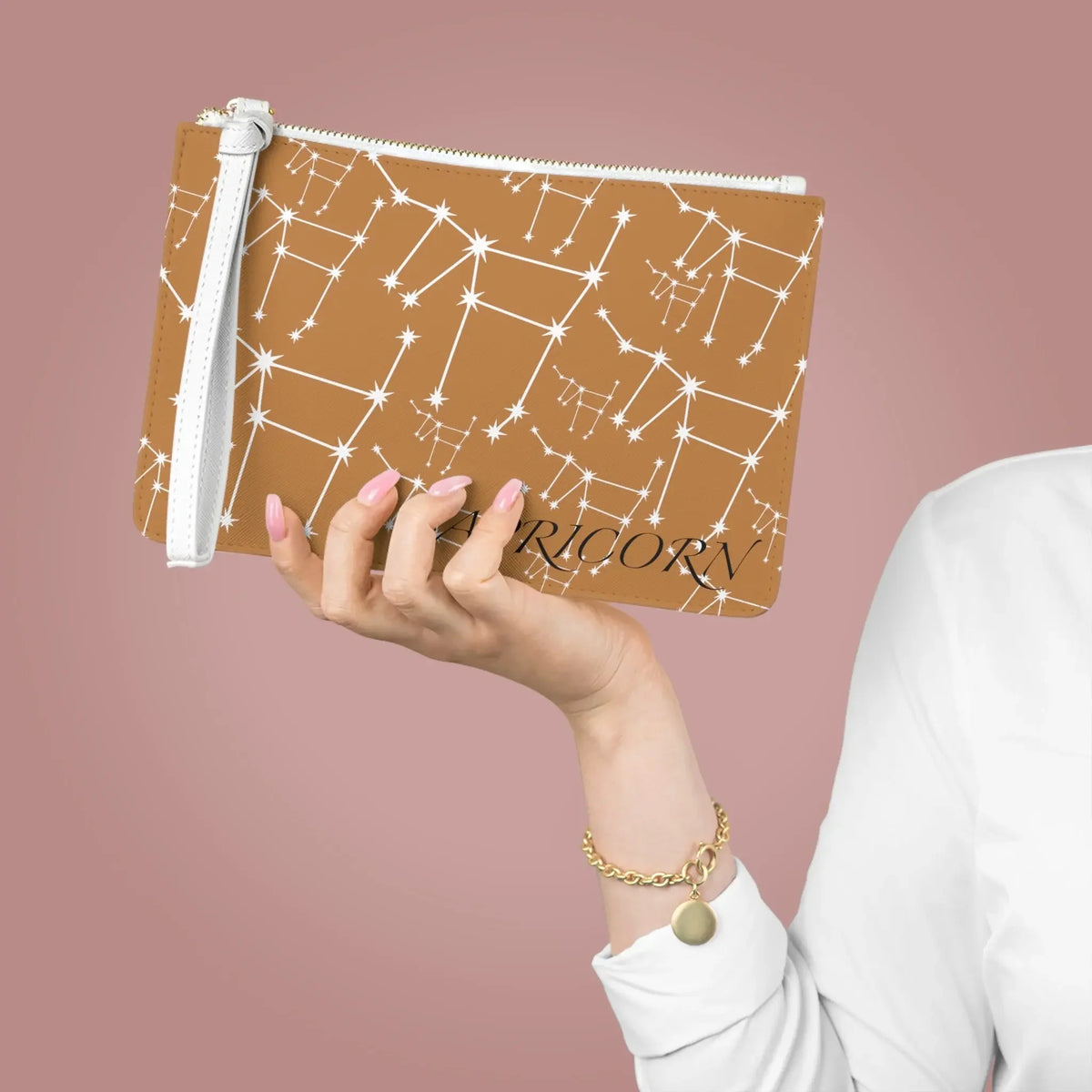 Tan zodiac pouch with white constellation stars and 'Capricorn' text, held by hand with pink nails.