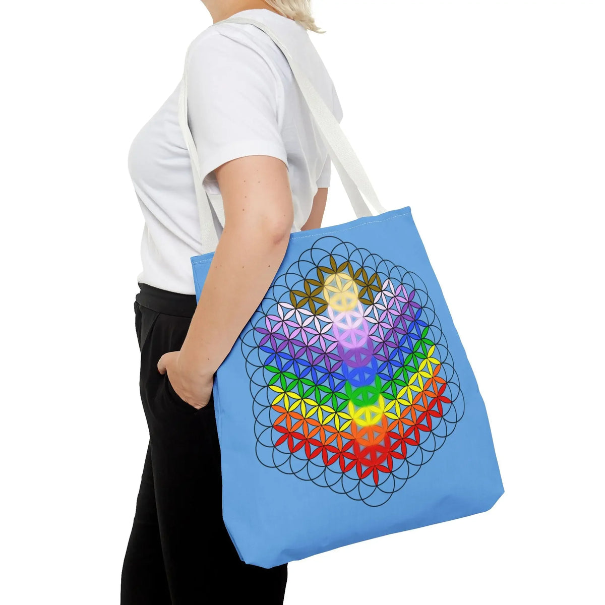 Blue tote bag with rainbow chakra flower of life design, carried by woman