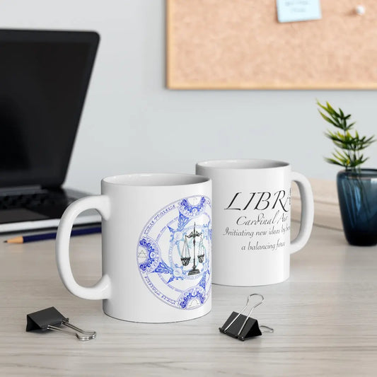 Two Libra Zodiac Mugs on a desk, showing both the quote side and the elemental sigil side.