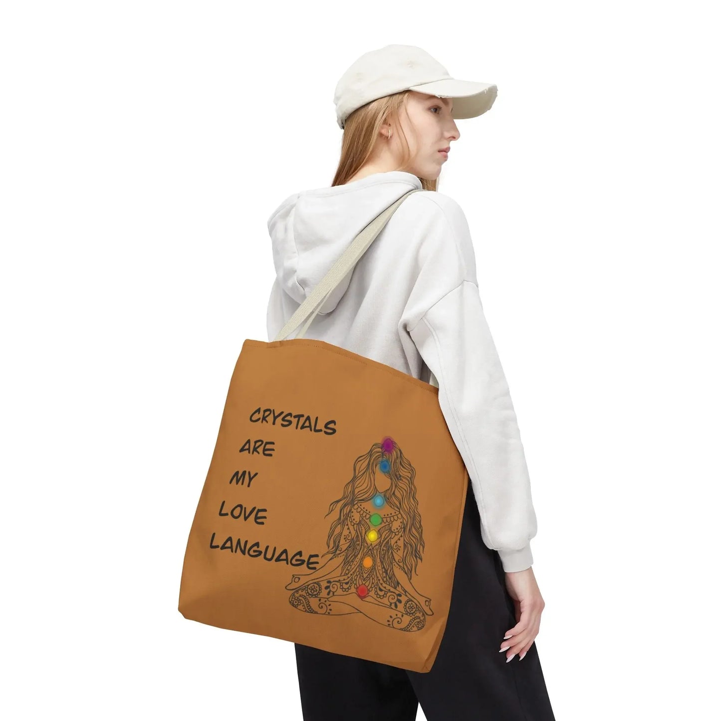 Brown tote bag with 'Crystals Are My Love Language' text and chakra design, worn by woman in white hoodie