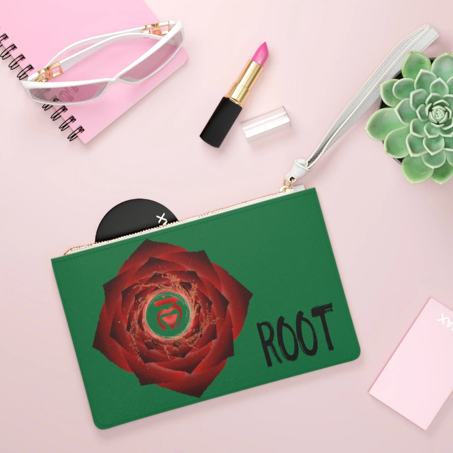 Root Chakra Clutch shown in a lifestyle setting with sunglasses and lipstick on a pink background.