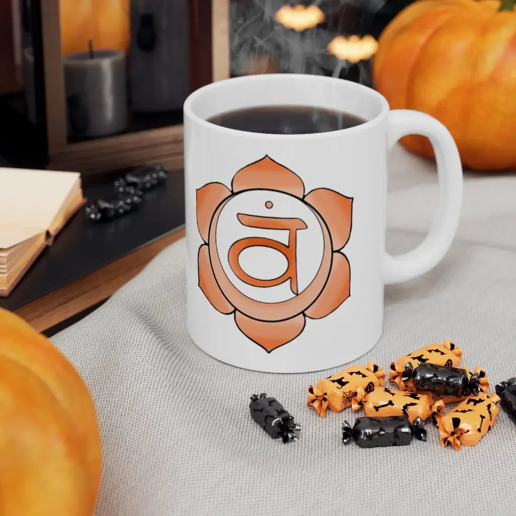 White mug with orange root chakra symbol, steaming coffee, Halloween candy, and pumpkins for spiritual wellness