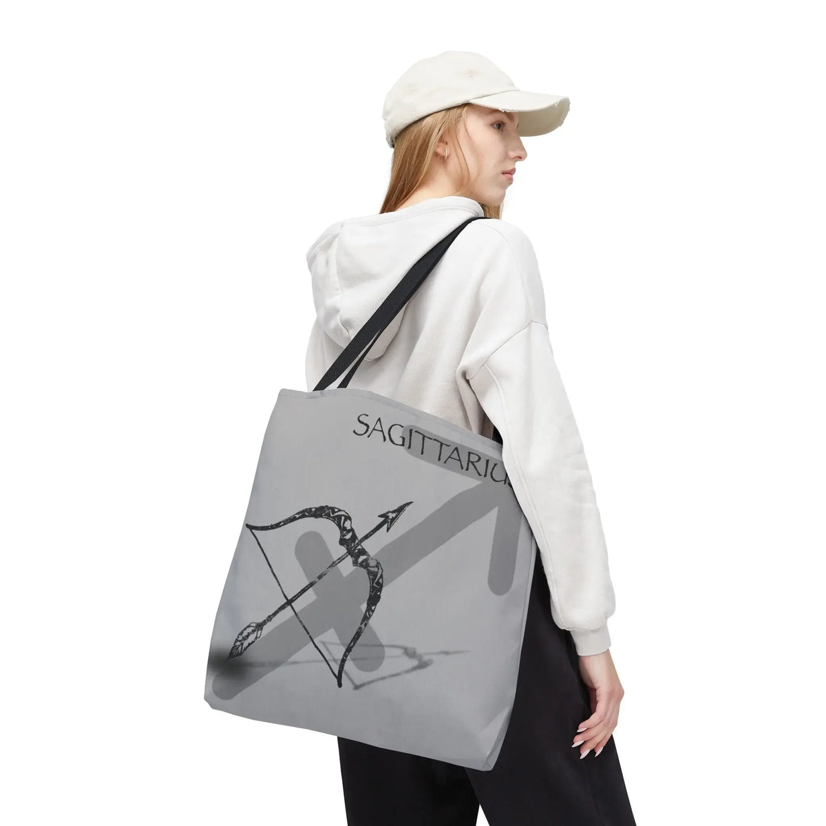 Gray Sagittarius tote bag with bow and arrow design, worn by woman in white hoodie and cap