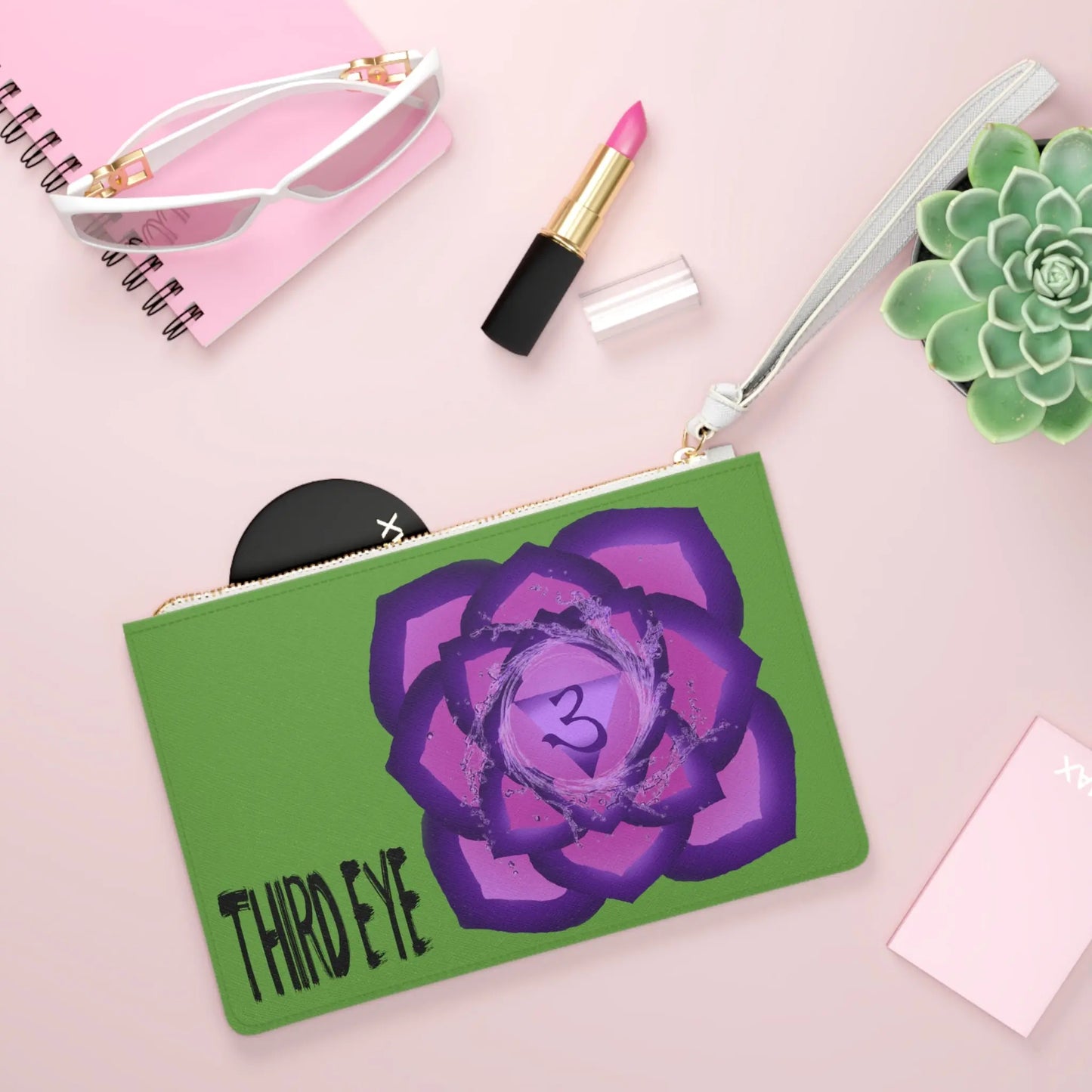 Third Eye Chakra Clutch shown in a lifestyle setting with sunglasses and lipstick on a pink background.