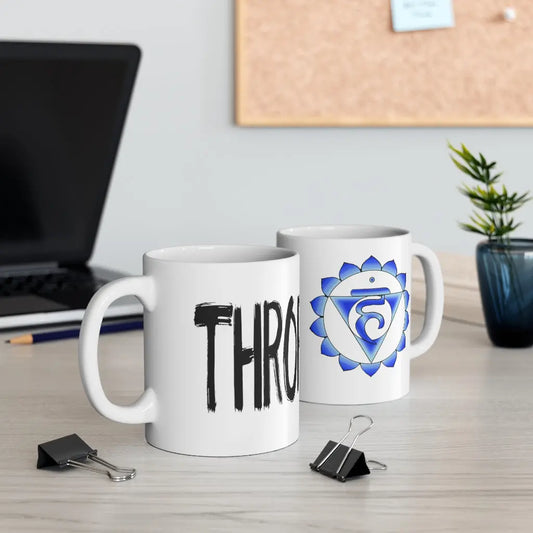 Two Throat Chakra Mugs on a desk, showing both the chakra symbol side and the "THROAT" text side.