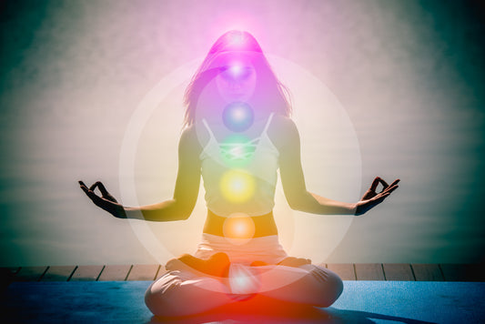A woman sits cross-legged in a yoga lotus pose in a serene natural setting. Her hands rest gently on her knees, and a soft glow surrounds her body, representing an aura.