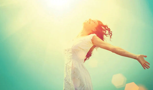 Woman embracing sunlight with open arms, radiating peace and energy for chakra healing and spiritual wellness