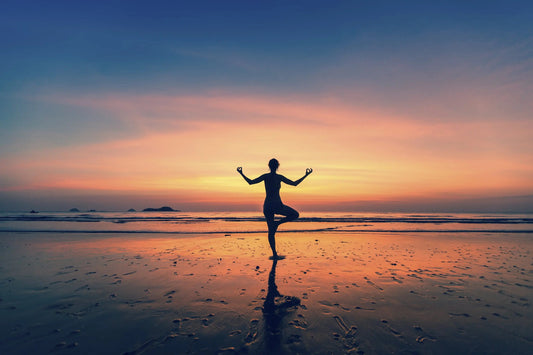 Silhouette of woman practicing tree pose yoga on beach at sunset, reflecting spiritual balance and chakra harmony