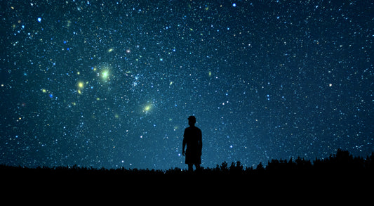 A man stands alone in a tranquil setting, gazing up at the starry night sky. The vast expanse is filled with countless stars, creating a breathtaking celestial view. 