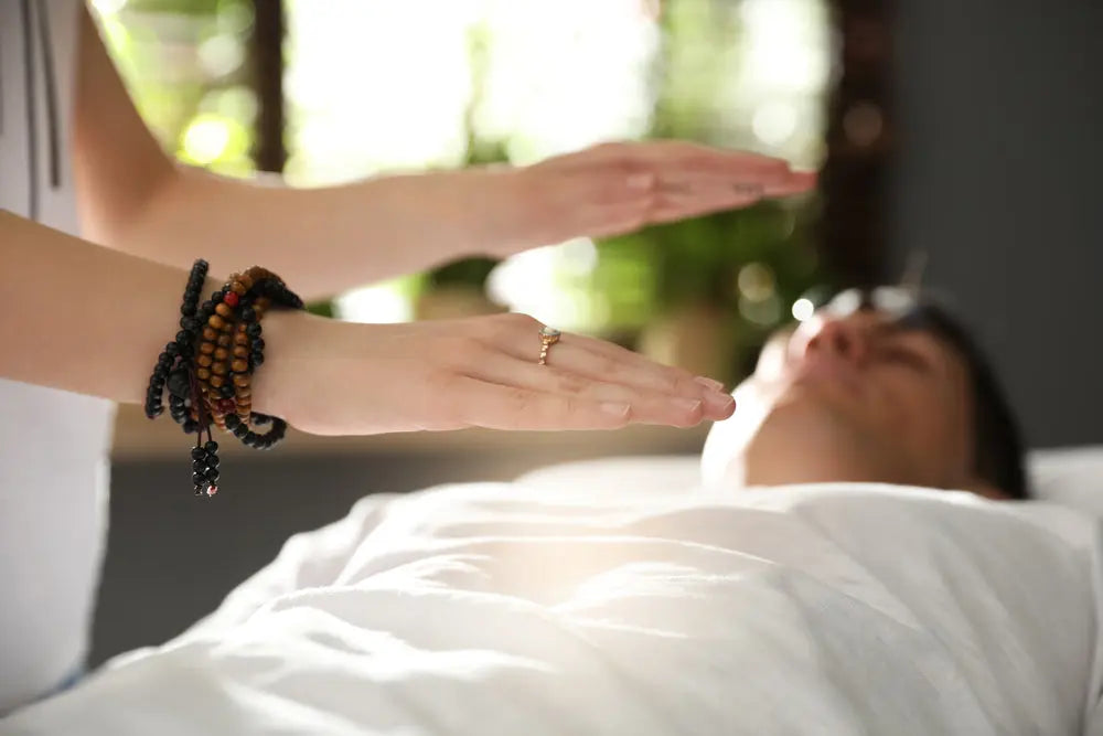 Healing hands hovering over person during chakra balancing session with beaded bracelets