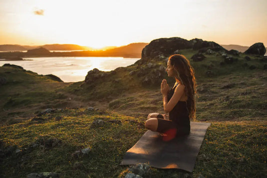 Woman meditating on yoga mat at sunset, practicing chakra alignment and mindfulness in nature